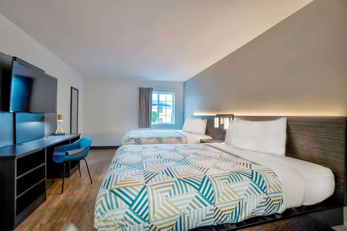 A hotel room with a large bed, a desk with a chair, a TV, and a window with curtains.