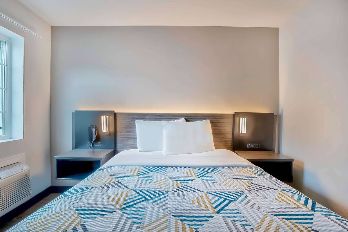 A hotel room with a large bed, two bedside tables, a heater, and a window.