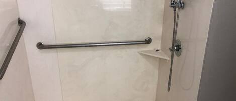 Eine begehbare Dusche mit Haltegriff, Duschkopf und Ablagefläche.