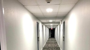 Un long couloir étroit, doté d’un tapis à motifs, de murs blancs et de portes de part et d’autre.