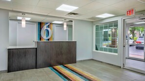 Un espace d’accueil comprenant un comptoir de réception, un grand panneau portant le chiffre « 6 », un tapis rayé aux couleurs vives et un panneau indiquant la sortie.