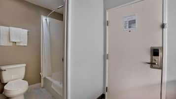 Baño con inodoro, ducha y bañera. Se observa una puerta con un cartel del plan de evacuación contra incendios.