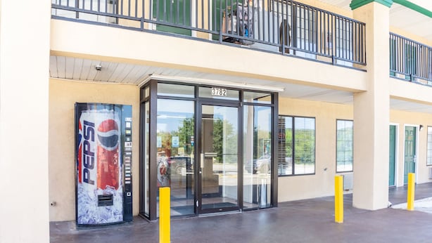 Entrada de um edifício com porta de vidro, uma máquina de refrigerantes Pepsi e um esperadizo amarelo.