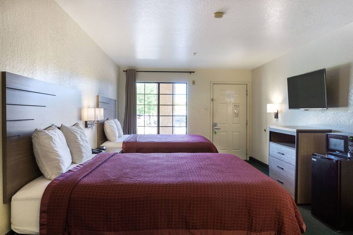 Une chambre d’hôtel avec deux lits, une télévision, un four à micro-ondes et une porte avec une fenêtre.