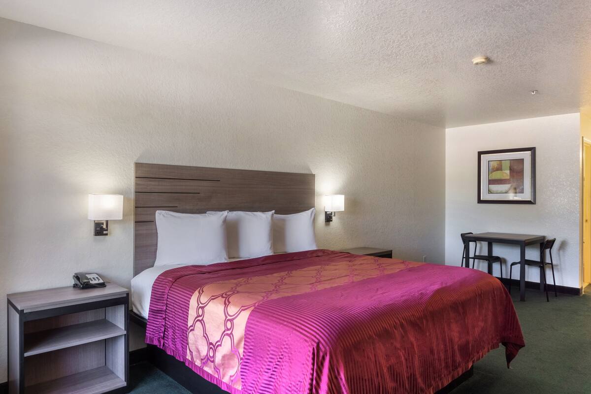 Une chambre d’hôtel avec un grand lit, deux lampes de chevet, une petite table avec des chaises et un tableau encadré au mur.