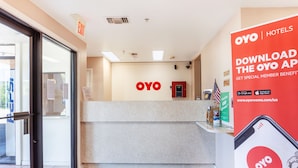 Uma área de recepção de hotel com entrada por porta de vidro, balcão de recepção e placa fixa na parede para o hotel OYO.