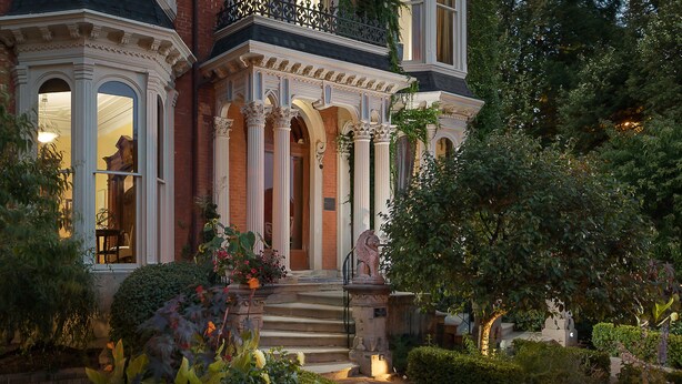 A grand entrance with a staircase leading to a door, surrounded by lush greenery and a well-maintained garden.