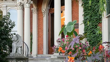 A historic building with ornate columns, a stone lion statue, and a variety of colorful flowers in the garden.