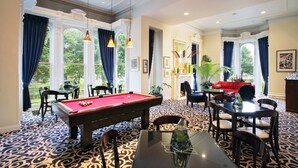 A pool table in a room with patterned carpet, a dining table with chairs, and a red sofa.