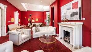 A living room with a red wall, white furniture, a fireplace, and a large abstract painting.