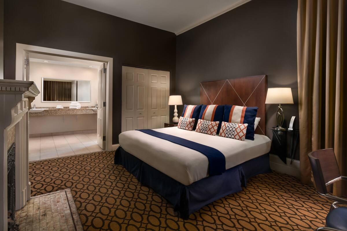 A hotel room with a large bed, a bathroom with a vanity, and a patterned carpet.