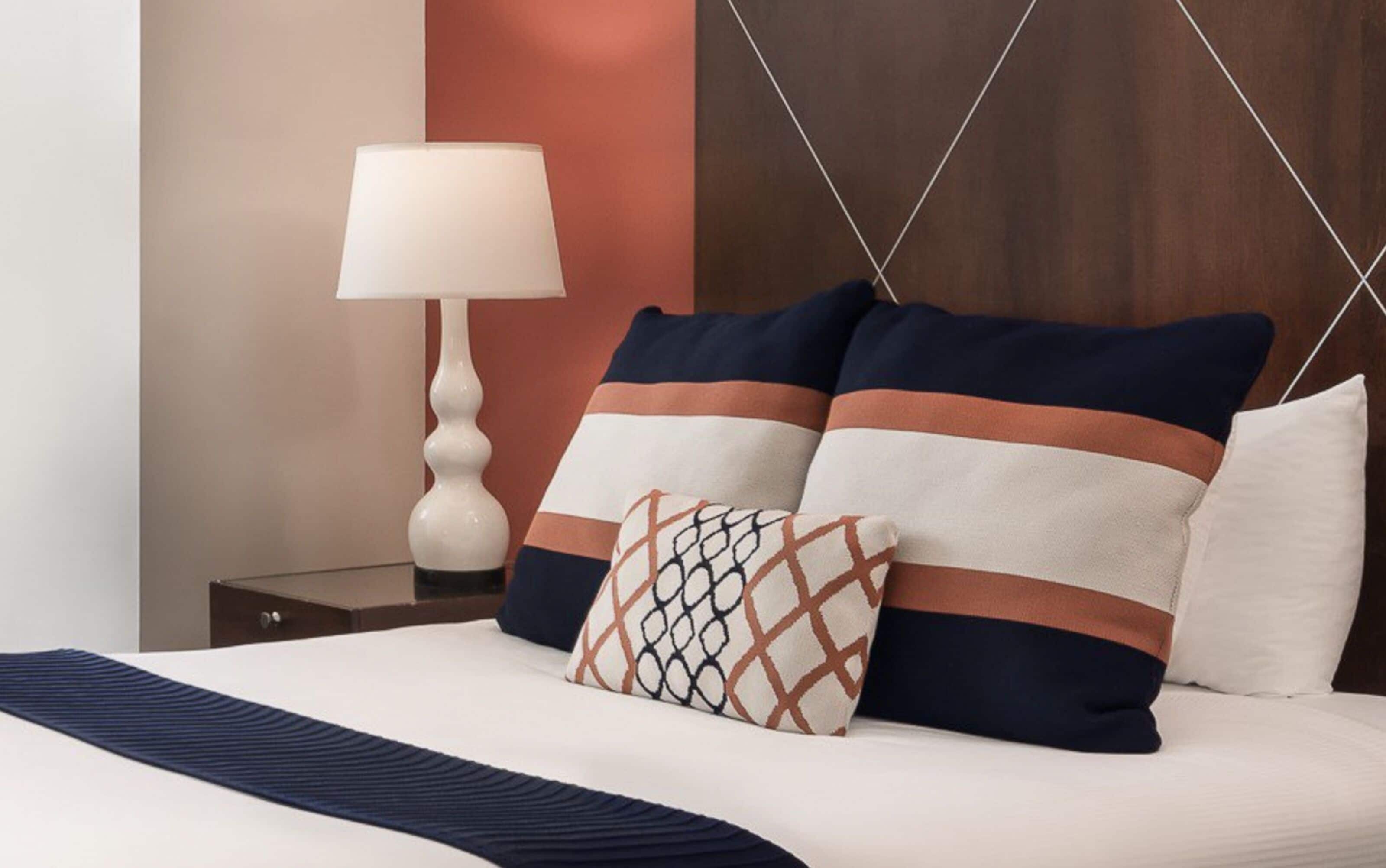 A neatly made bed with a patterned pillow, a bedside table with a lamp, and a wooden headboard.