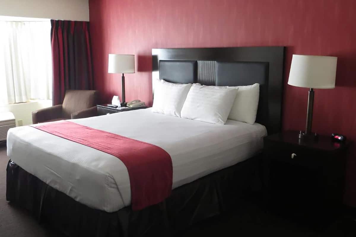 A hotel room with a large bed, a chair, two bedside tables, and a window with curtains.