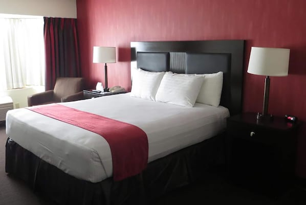 A hotel room with a large bed, a chair, two bedside tables, and a window with curtains.