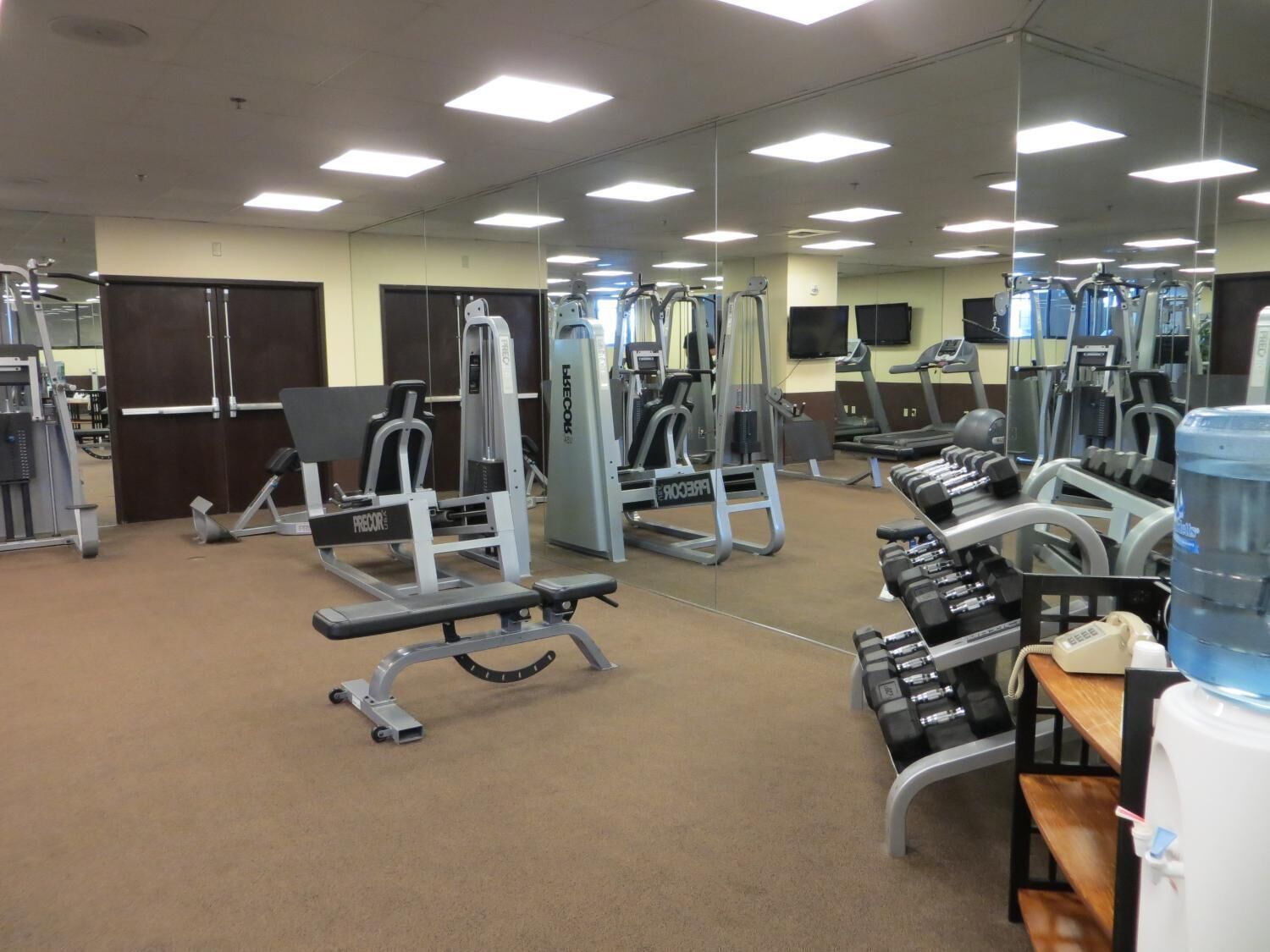 Un gimnasio con varios equipos de ejercicio, incluyendo mancuernas, una banca y máquinas de pesas.