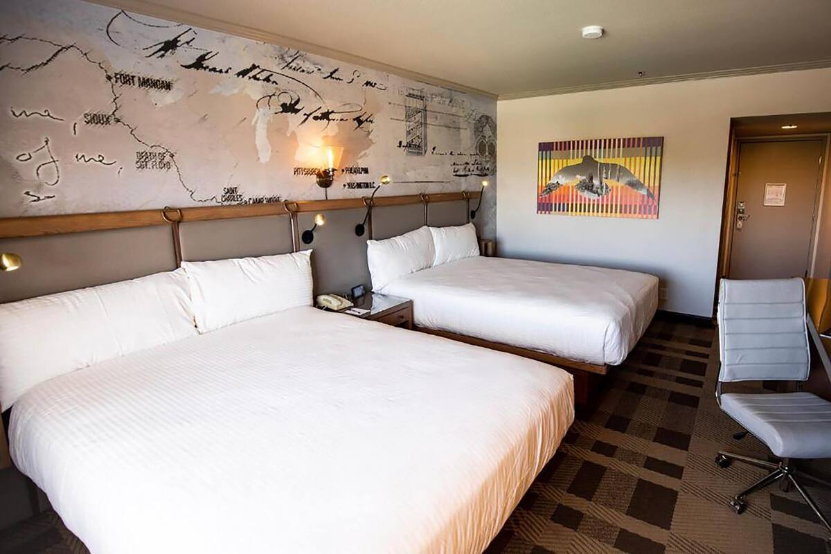 A hotel room with two beds, a desk, a chair, a map on the wall, and a painting.