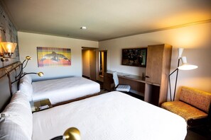 A hotel room with two beds, a desk, a chair, and a TV.