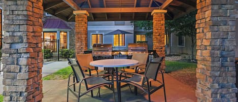 An outdoor patio with a round table and chairs, a grill, and stone pillars.