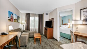 A hotel room with a sofa, a small table, a TV, a desk with a phone, and a bed. - Staybridge Suites Round Rock by IHG (Round Rock)