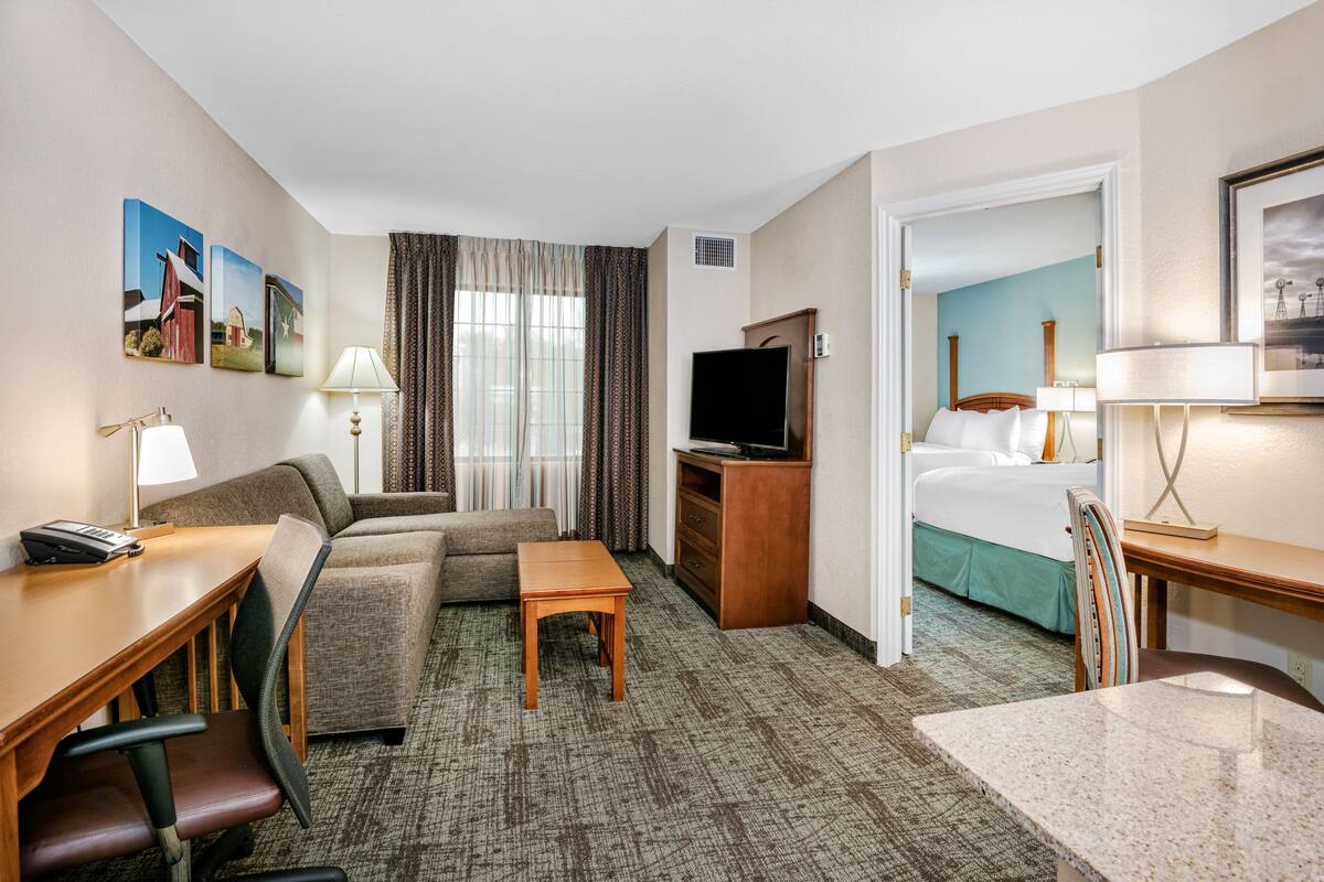 A hotel room with a sofa, a small table, a TV, a desk with a phone, and a bed.