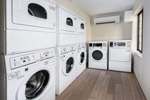A laundry room with stacked washers and dryers, a wooden floor, and an air conditioning unit on the wall. - Staybridge Suites Round Rock by IHG (Round Rock)