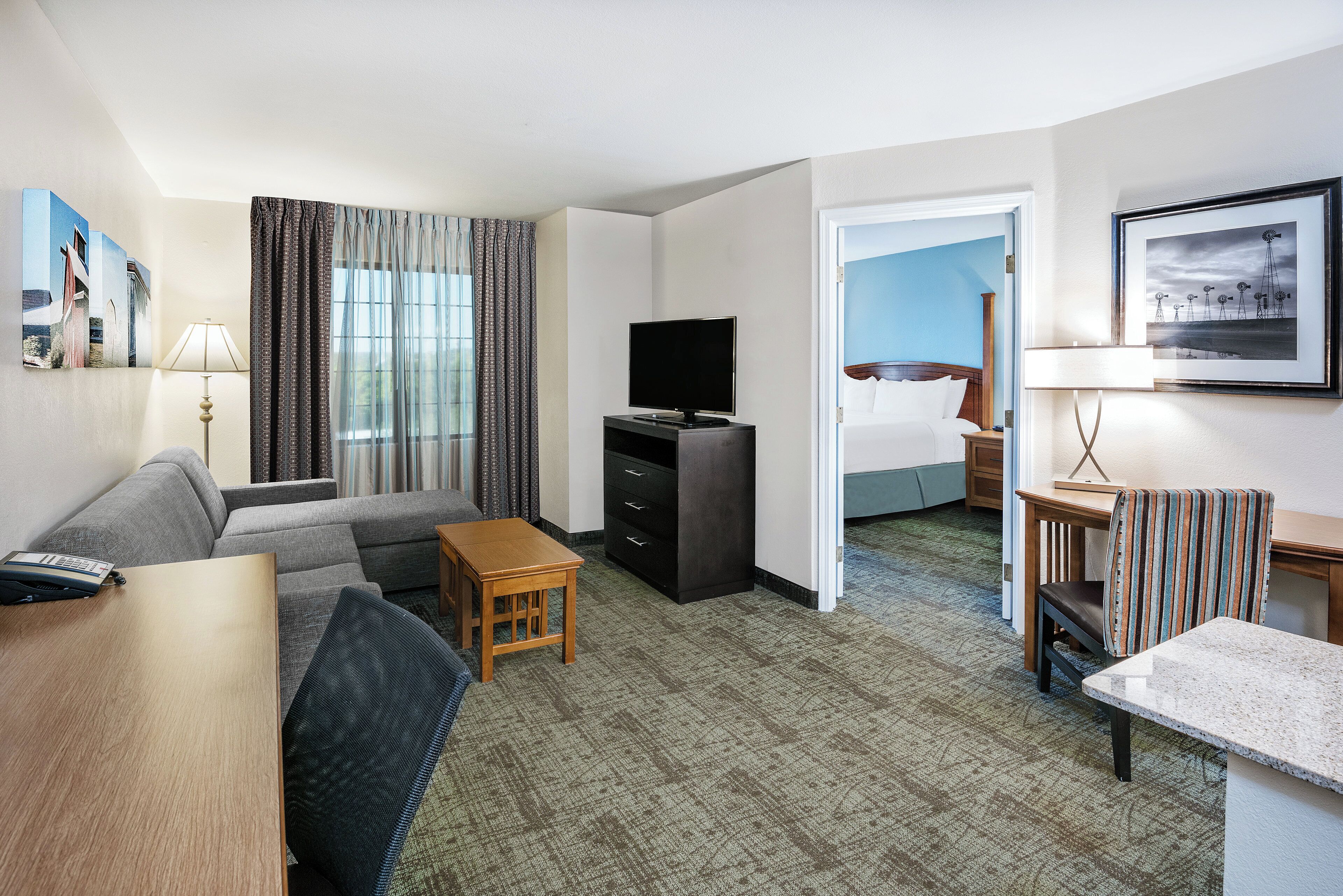 A hotel room with a sofa, a TV, a small table, a desk, and a bed.