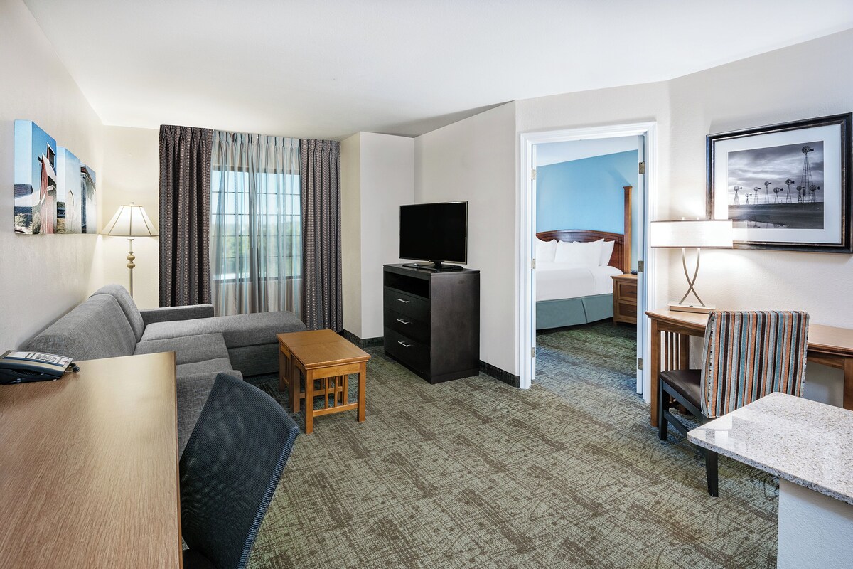 A hotel room with a sofa, a TV, a small table, a desk, and a bed.