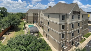 A multi-story hotel with a swimming pool, outdoor seating, and a well-maintained lawn.