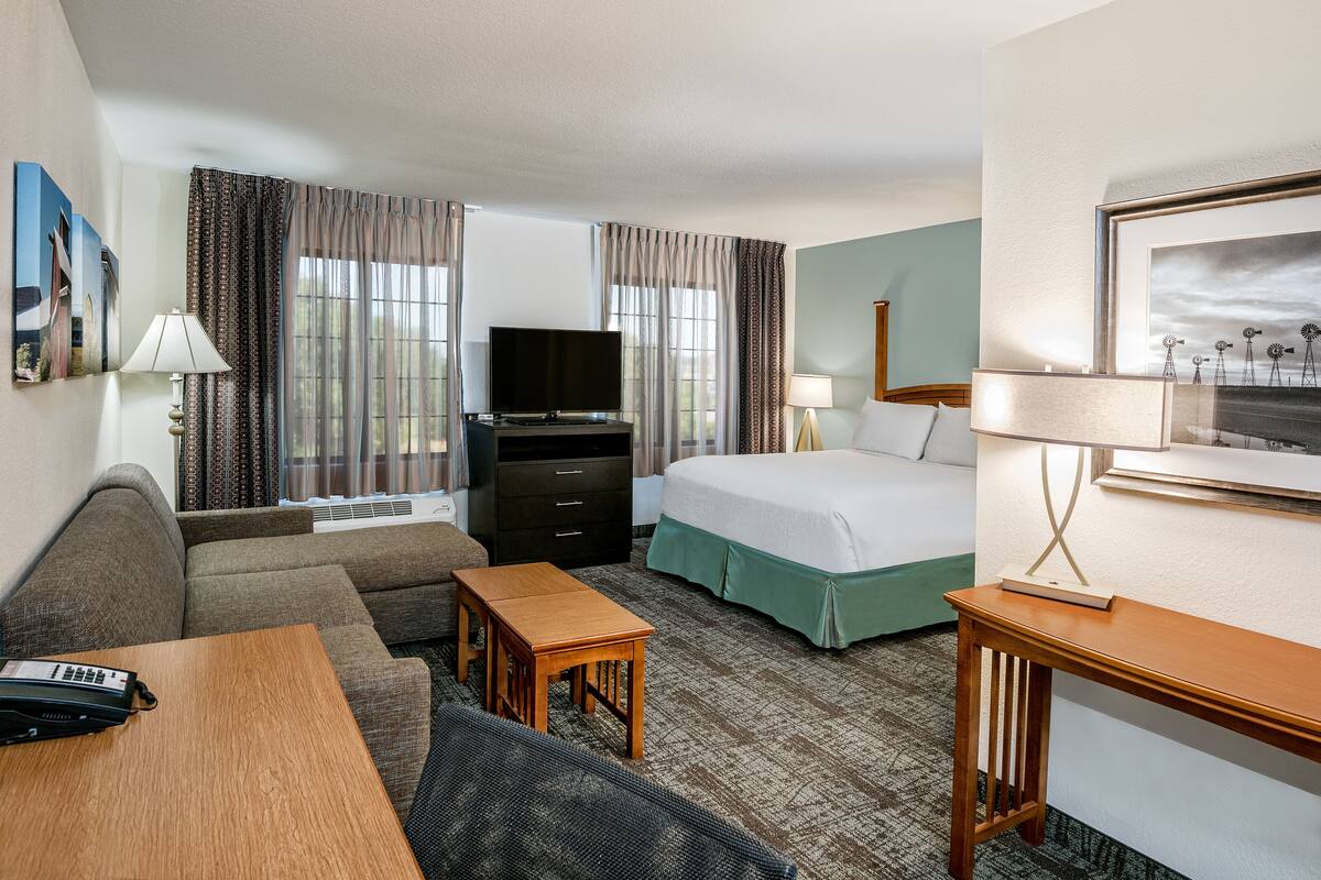 A hotel room with a sofa, a bed, a desk, a television, and a window with curtains.
