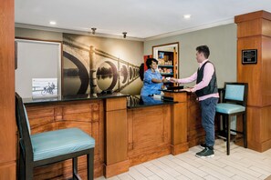 A reception area with a wooden counter, a seating area with a blue chair, and a wall with a bridge mural. - Staybridge Suites Round Rock by IHG (Round Rock)
