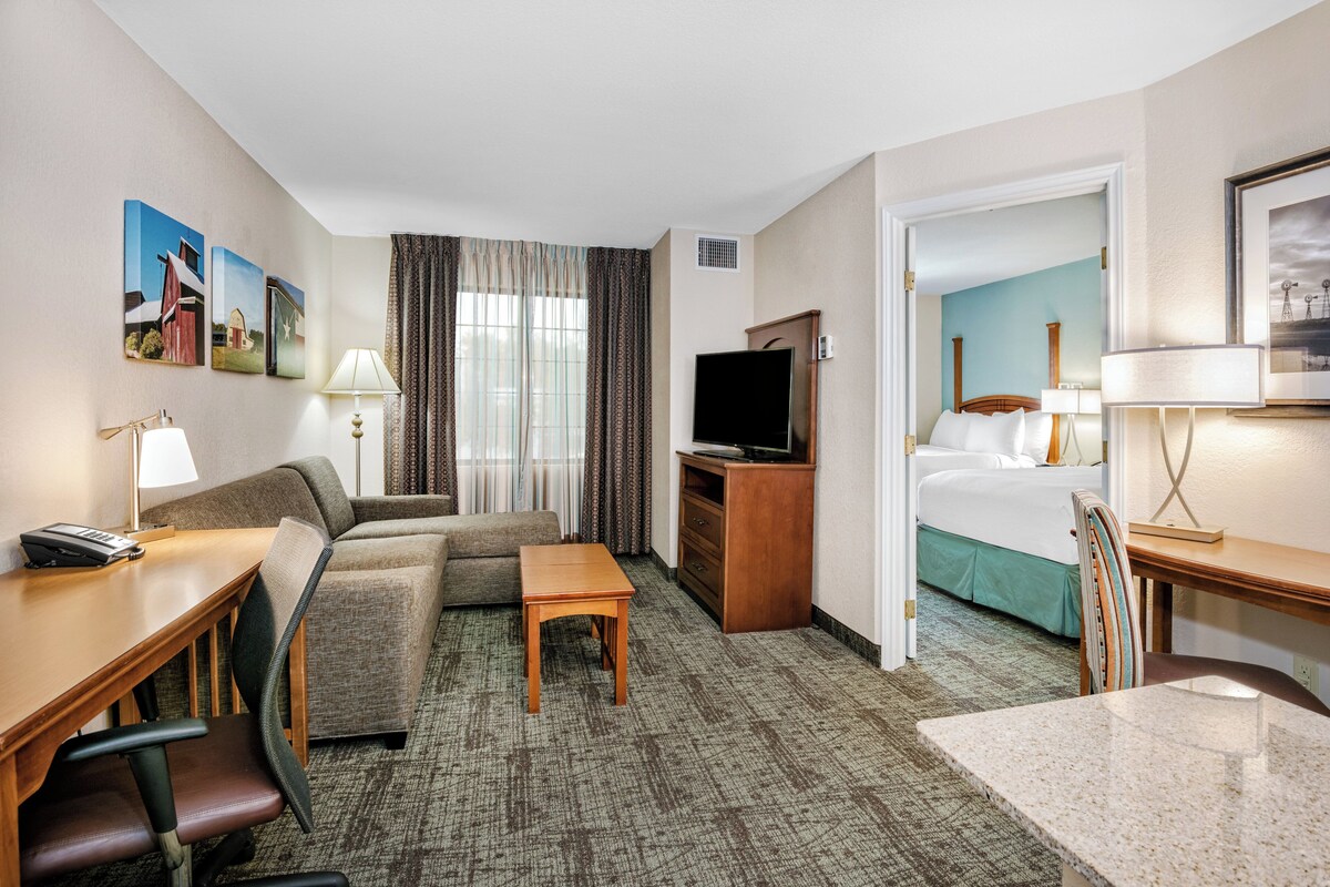 A hotel room with a sofa, a small table, a TV, a desk with a phone, and a bed.