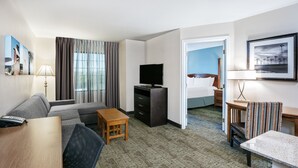 A hotel room with a sofa, a TV, a small wooden table, a desk, and a chair. There is a bed in the background. - Staybridge Suites Round Rock by IHG (Round Rock)