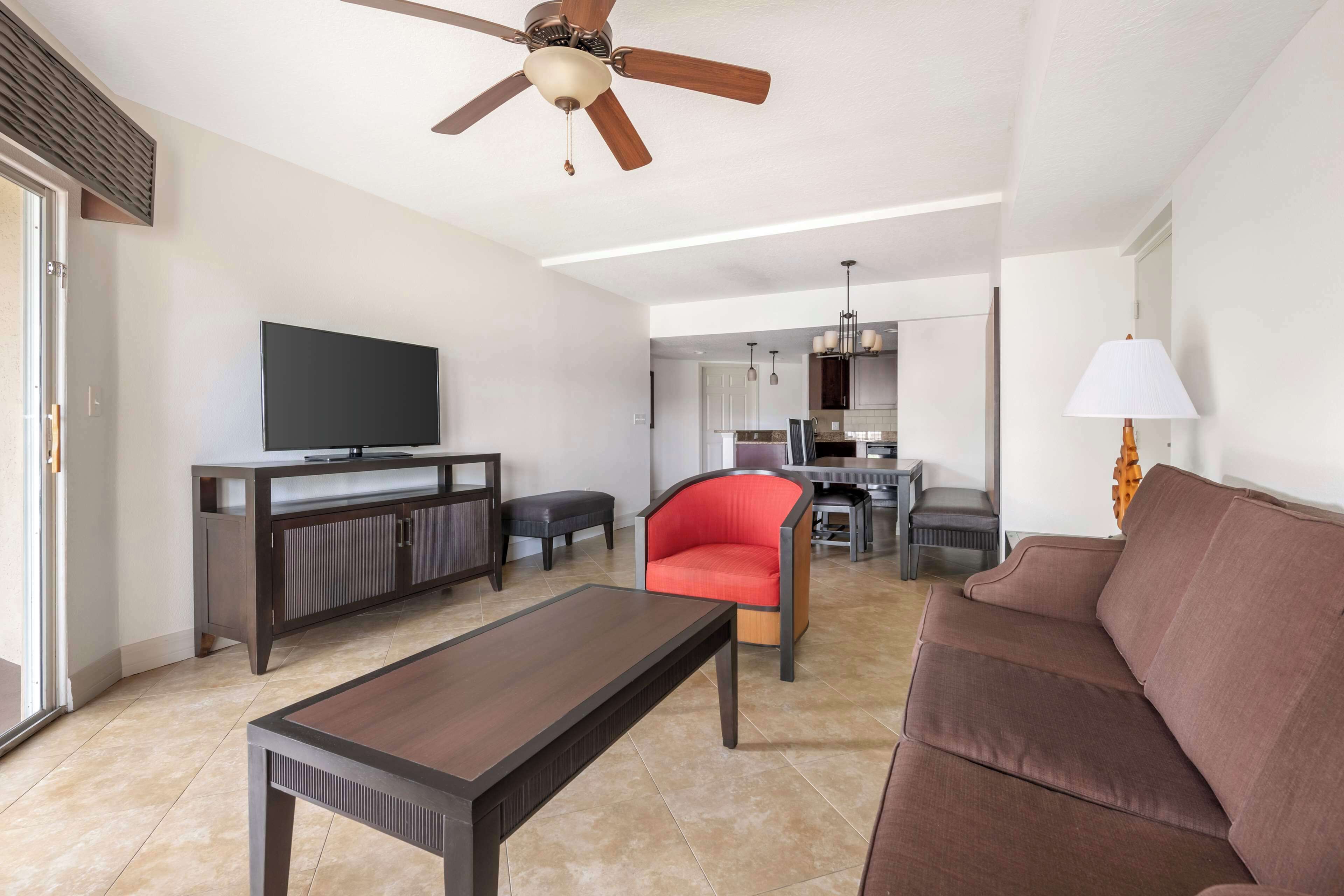 Una sala de estar moderna con un televisor de pantalla plana, una mesa de centro de madera, un sillón rojo, un sofá marrón y un ventilador de techo.