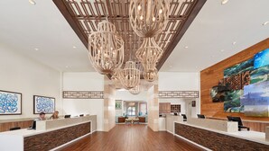 Un vestíbulo amplio con mostrador de recepción, suelo de madera y candelabros modernos.