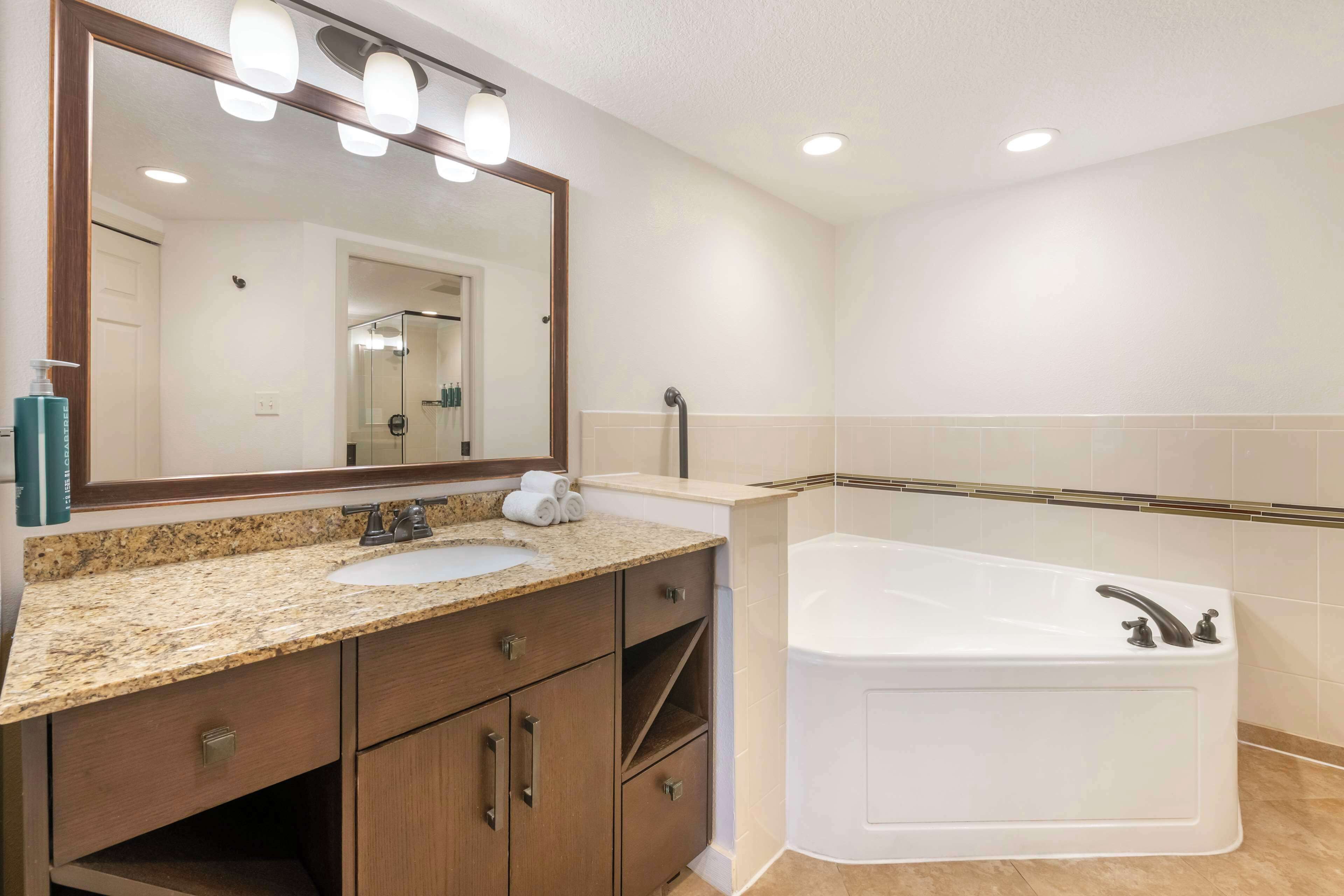 Un baño con un espejo grande, un lavabo, una bañera y armarios de madera.