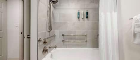 A modern bathroom with a bathtub, shower, and handrails.