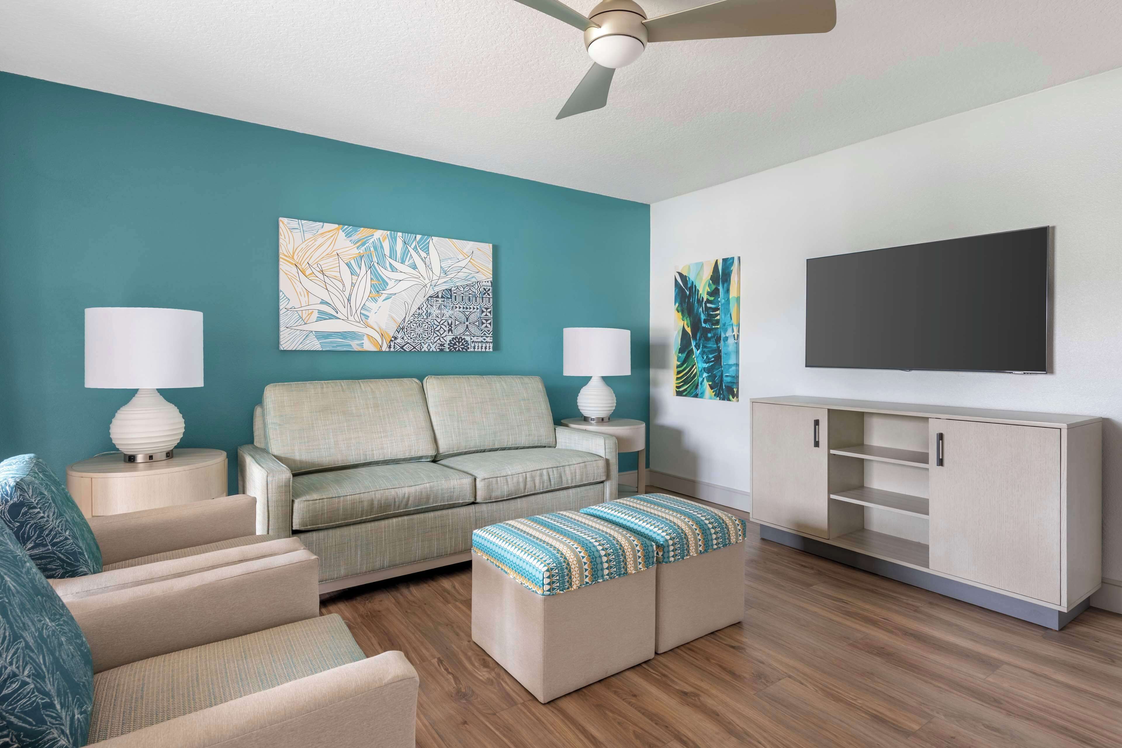 A living room with teal walls, a sofa, two armchairs, a coffee table, a TV, and a cabinet.