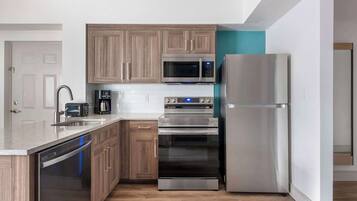 A modern kitchen with wooden cabinets, stainless steel appliances including a microwave, oven, and refrigerator, and a dishwasher.