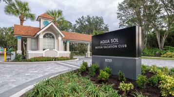 The exterior of the Aqua Sol Hilton Vacation Club, featuring a modern building with a tiled roof, a covered entrance, and a landscaped garden area with various plants and a signboard.
