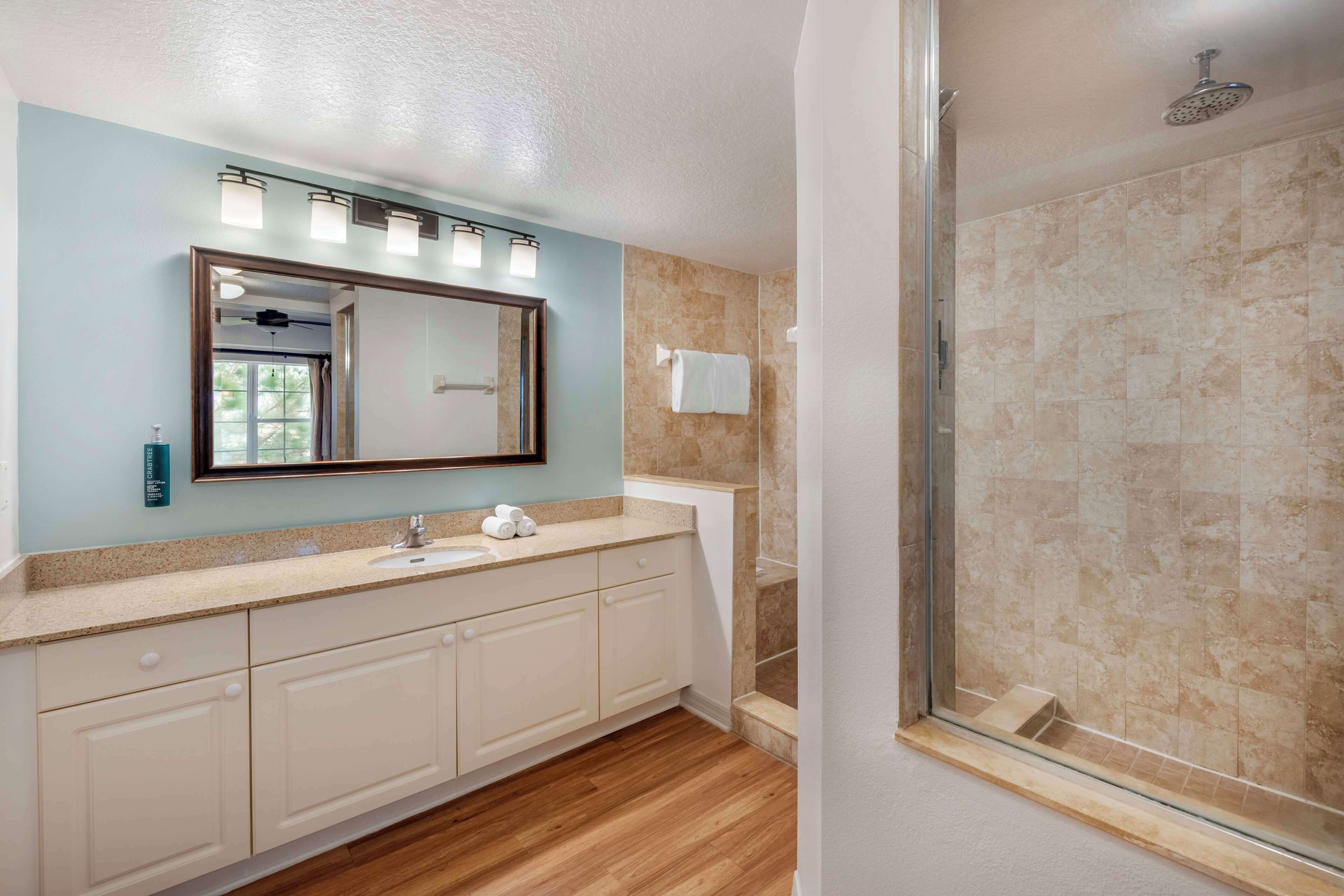 Un baño con un espejo grande, un lavamanos y una ducha.