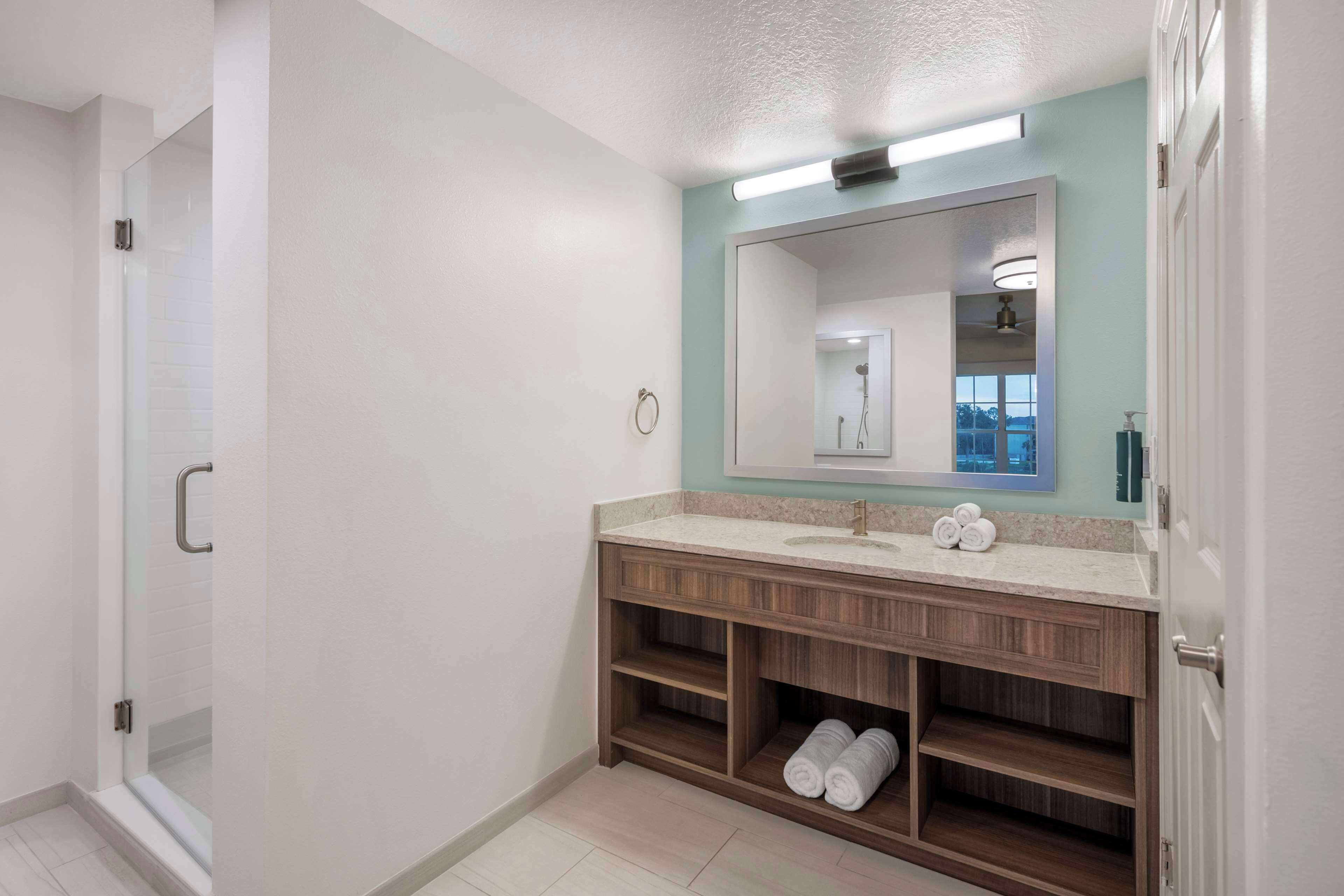 Un baño moderno con ducha, lavabo con espejo y estantes empotrados para toallas.