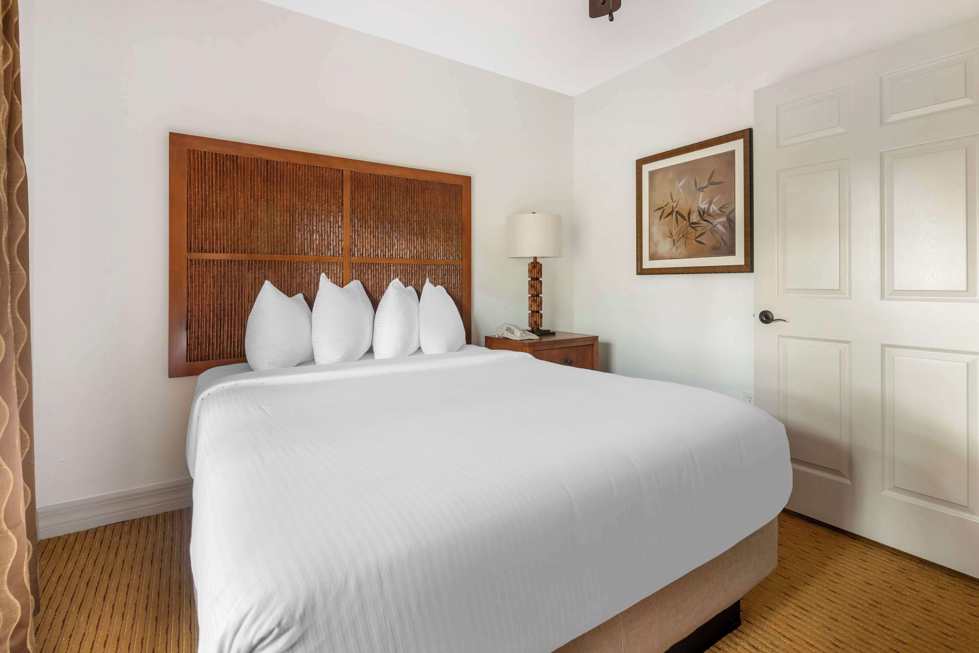 Ein Hotelzimmer mit einem großen Bett, einem hölzernen Kopfteil, einem Nachttisch mit Lampe und einem gerahmten Bild an der Wand.