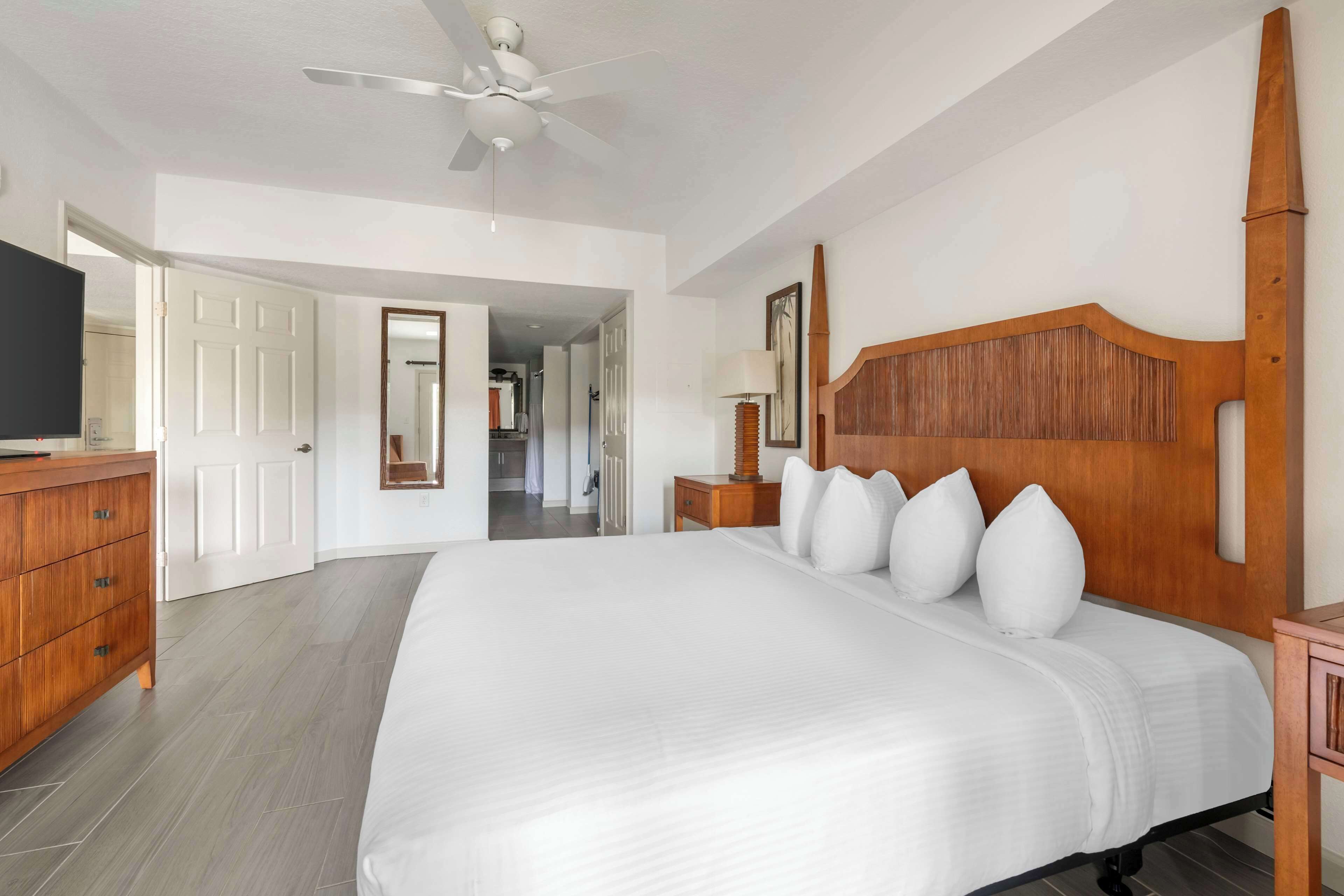 A spacious bedroom with a large bed, wooden headboard, and a ceiling fan.