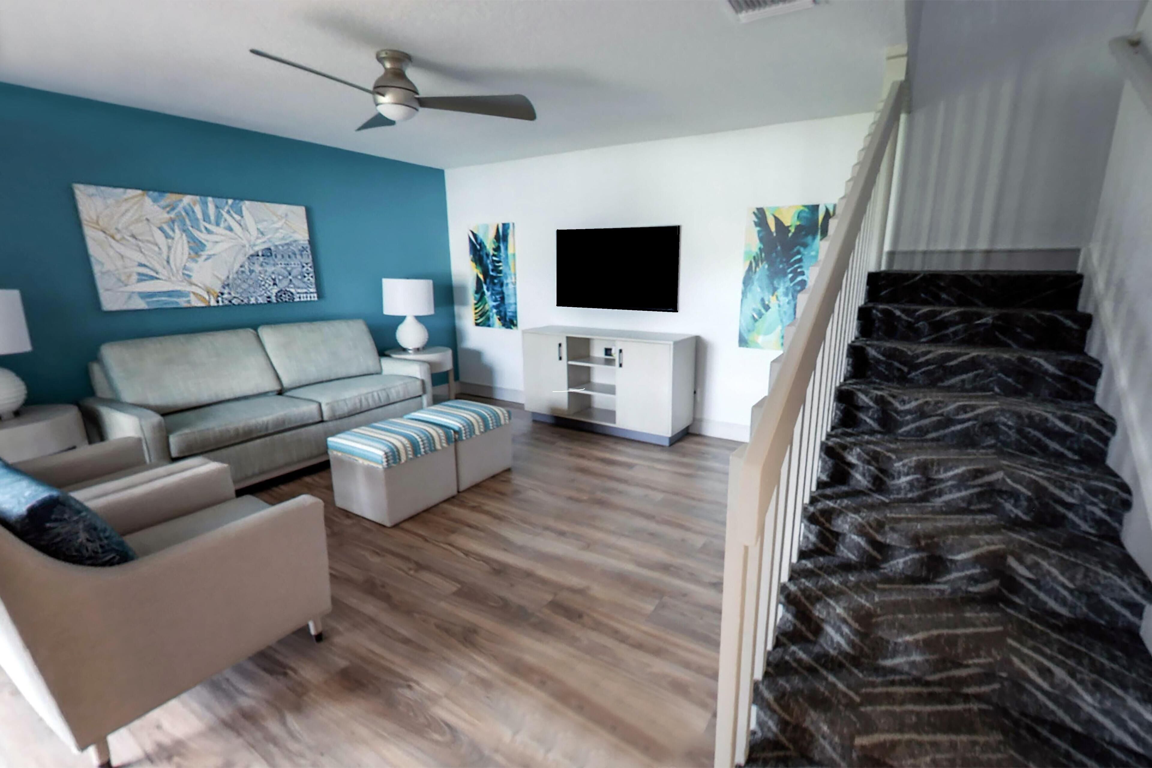 A living room with a sofa, ottoman, TV, and artwork on the walls.