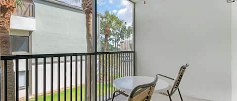 A balcony with a table and chairs, a ceiling fan, and a view of palm trees and a building.