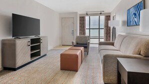 Habitación de hotel moderna con televisión de pantalla plana, sofá, sillón y una ventana grande con vistas.