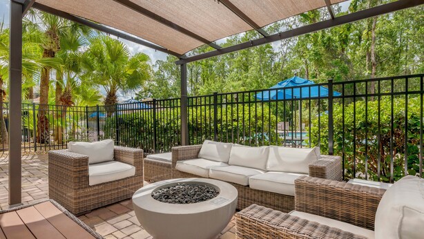Un patio al aire libre con mobiliario de mimbre, una chimenea y vistas a una piscina y vegetación.
