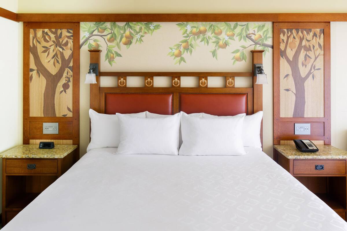 Een hotelkamer met een groot bed, twee nachtkastjes, een houten hoofdbord met afbeeldingen van fruitbomen en een aan de muur bevestigde telefoon.