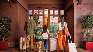 Una familia con maletas en la entrada de un hotel con fachada de madera y ventanas de vidrio emplomado.