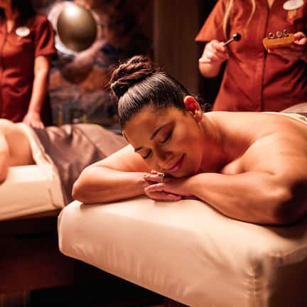 A massage therapy room with two massage tables and a wooden wall.
